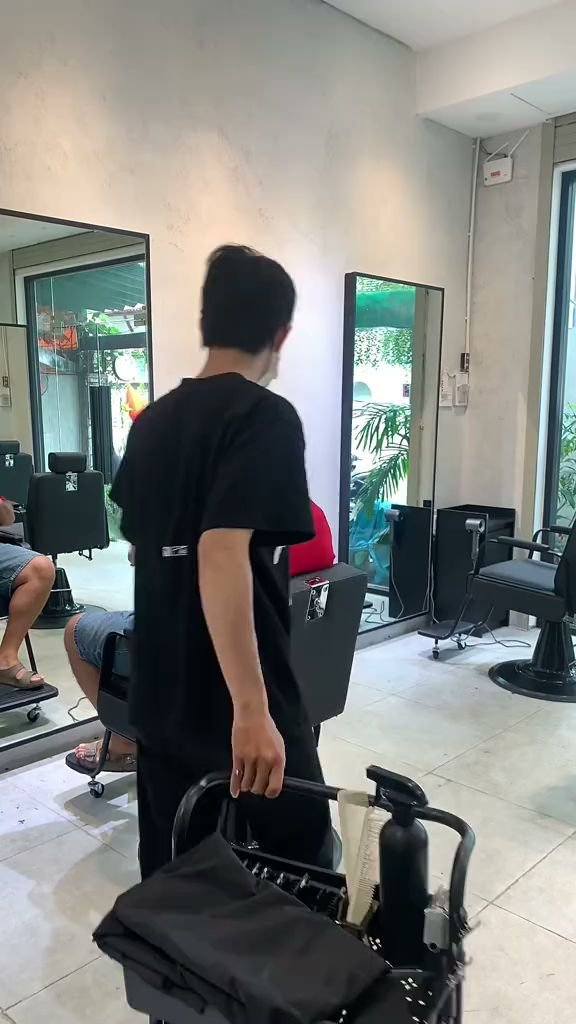 A person is walking through a modern hair salon or barber shop interior. The individual appears to be moving towards the back of the room, possibly he