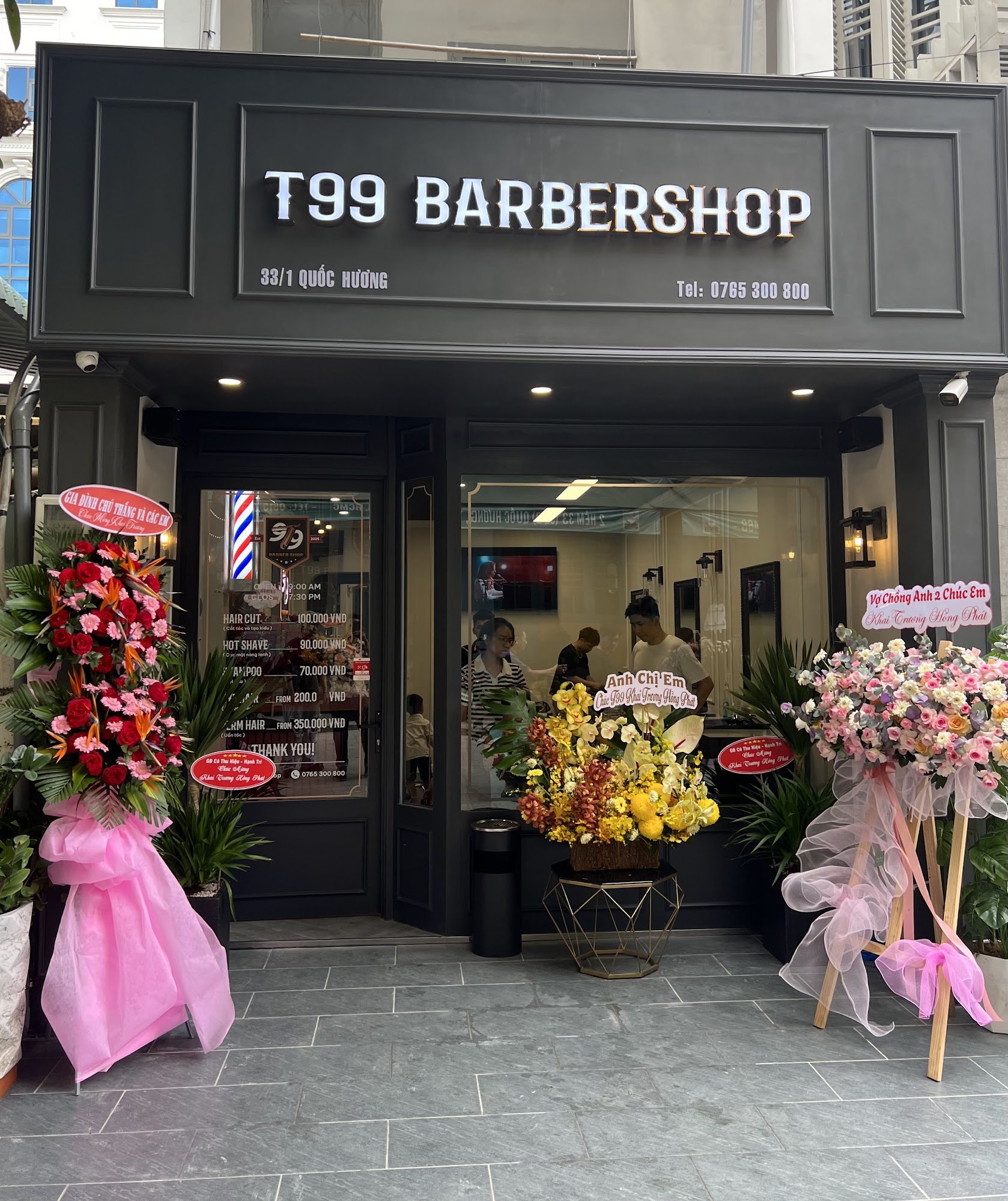 The image shows an exterior view of a barber shop named 'T99 Barbershop' located at Quoc Huong street, District One in Saigon.