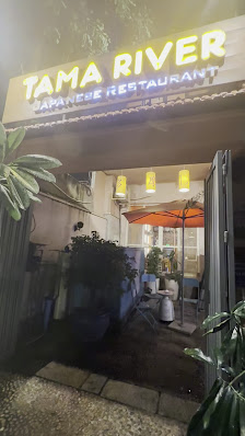 The image shows an exterior view of a Japanese restaurant named 'TAMA RIVER' with outdoor seating visible through the open door.