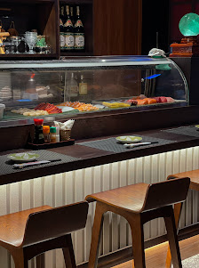 The image shows a modern interior of what appears to be a sushi bar or restaurant with a curved counter displaying various food items and condiments,
