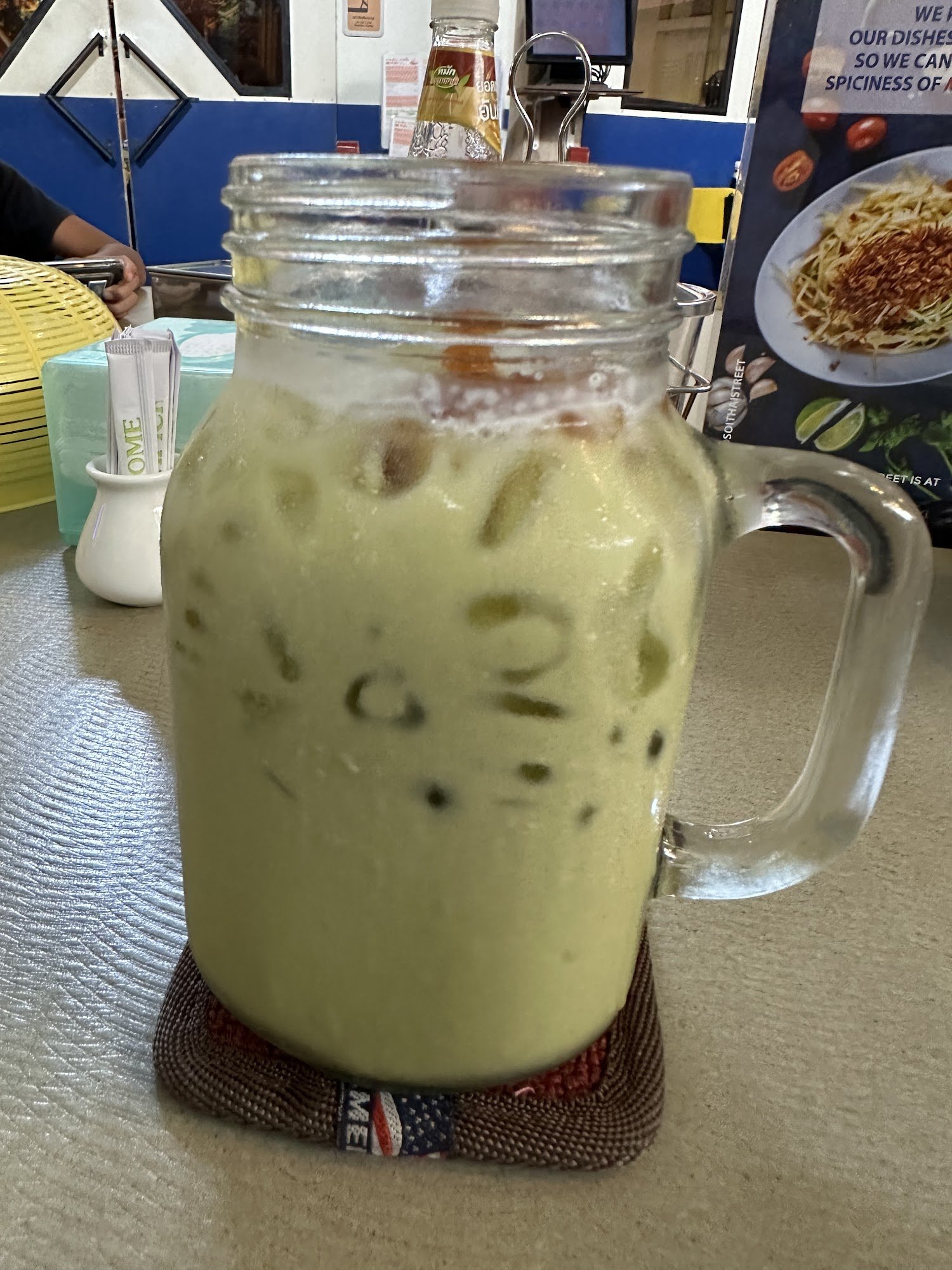 A glass jar filled with a green-colored beverage that appears thick and creamy, possibly containing tapioca pearls or similar ingredients floating wit