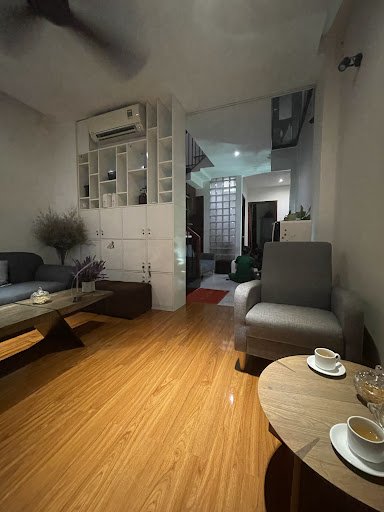 The image shows a modern living room interior featuring wooden flooring and contemporary furniture including sofas, chairs, coffee tables, and shelvin