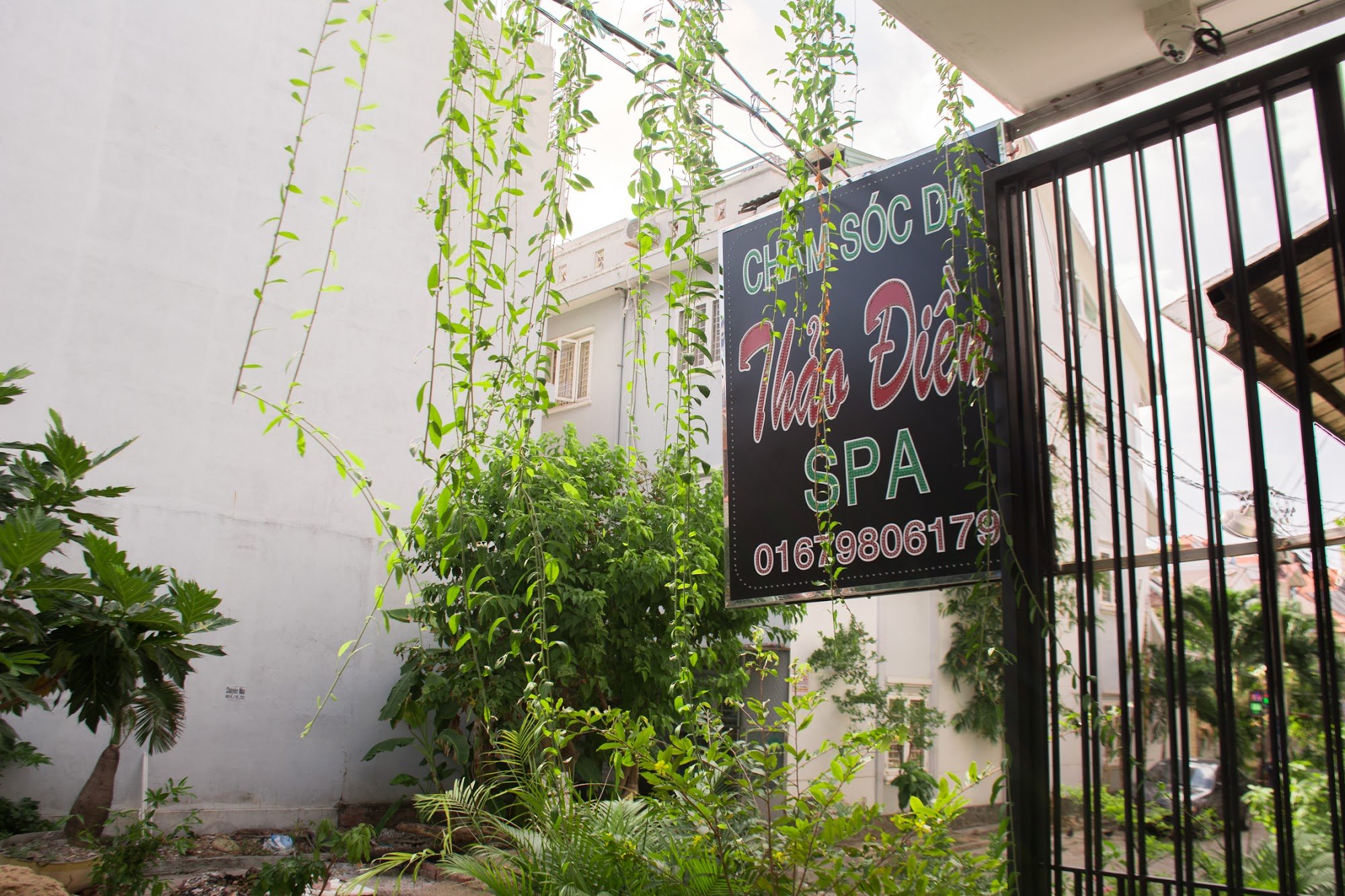 The image depicts the exterior of a spa named 'Thảo Điền SPA' located in Thao Dien, Saigon. A black signboard with green and red text displays 'CHĂM S