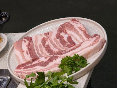 A close-up of a plate containing slices of raw bacon garnished with fresh parsley and cilantro.