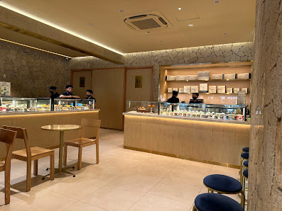 The image shows an interior view of a modern cafe or dessert shop in Thao Dien, Saigon. The decor features warm tones with wooden elements and stone w