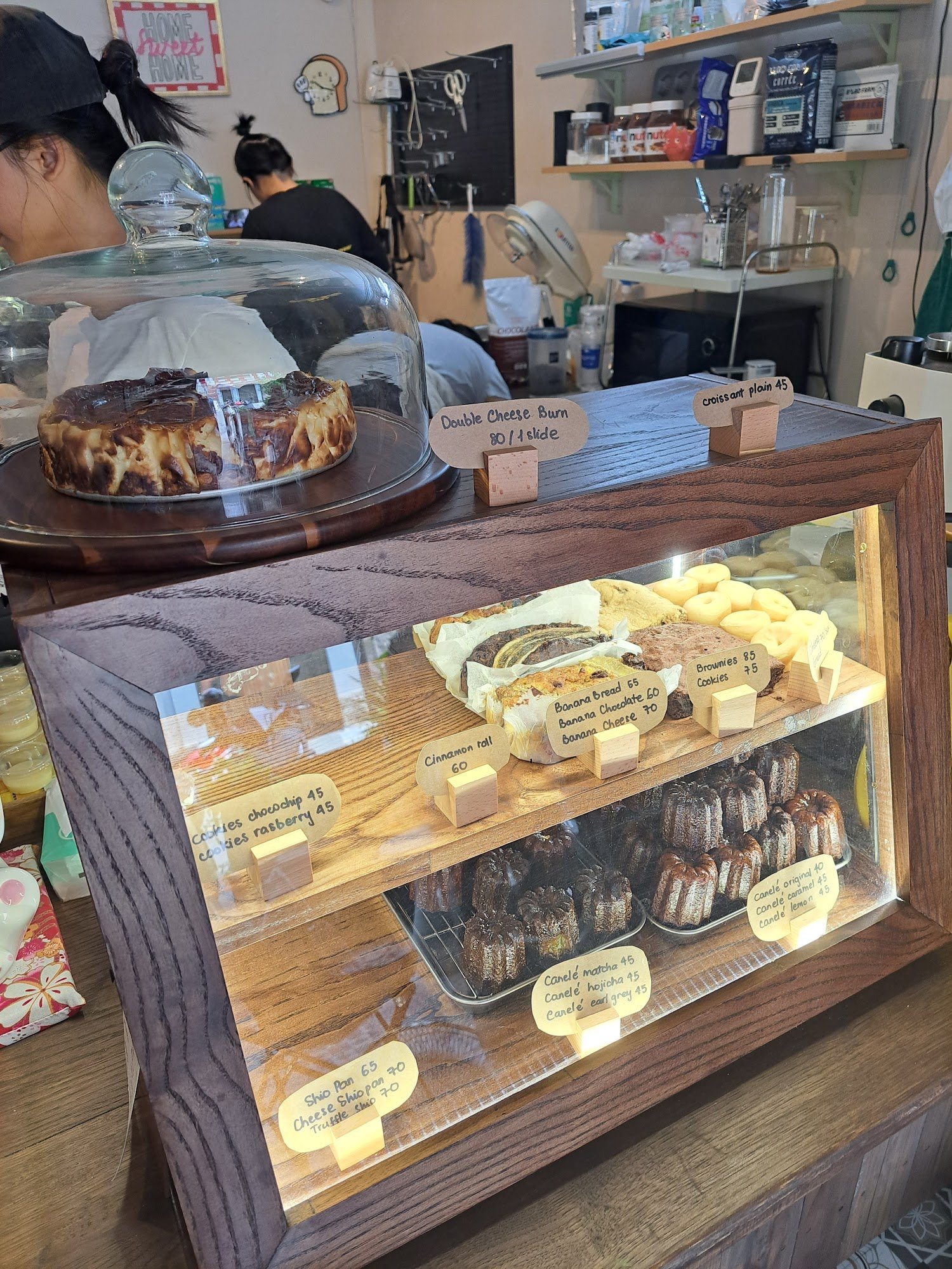 The image shows a display case in an interior setting of what appears to be a bakery or café. The glass dome on the left contains a baked item, possib