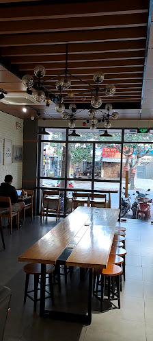The image shows an interior view of a modern cafe or restaurant in Thao Dien, Saigon. The space features wooden slatted ceilings and large windows tha