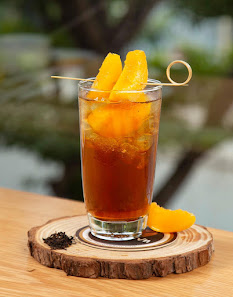 A glass of amber-colored cocktail garnished with orange slices and a skewer containing two pieces of fruit on top.