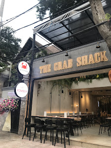 The image depicts the exterior of 'THE CRAB SHACK,' a restaurant in Thao Dien, Saigon. It features a modern facade with large glass windows revealing 