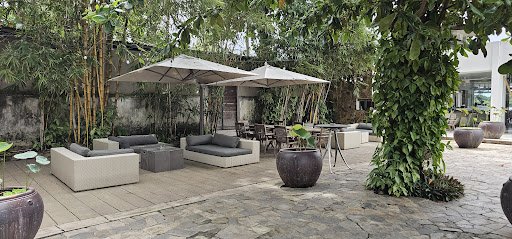 The image depicts an outdoor seating area of a venue in Thao Dien, Saigon. It features modern, minimalist lounge furniture including square sofas and