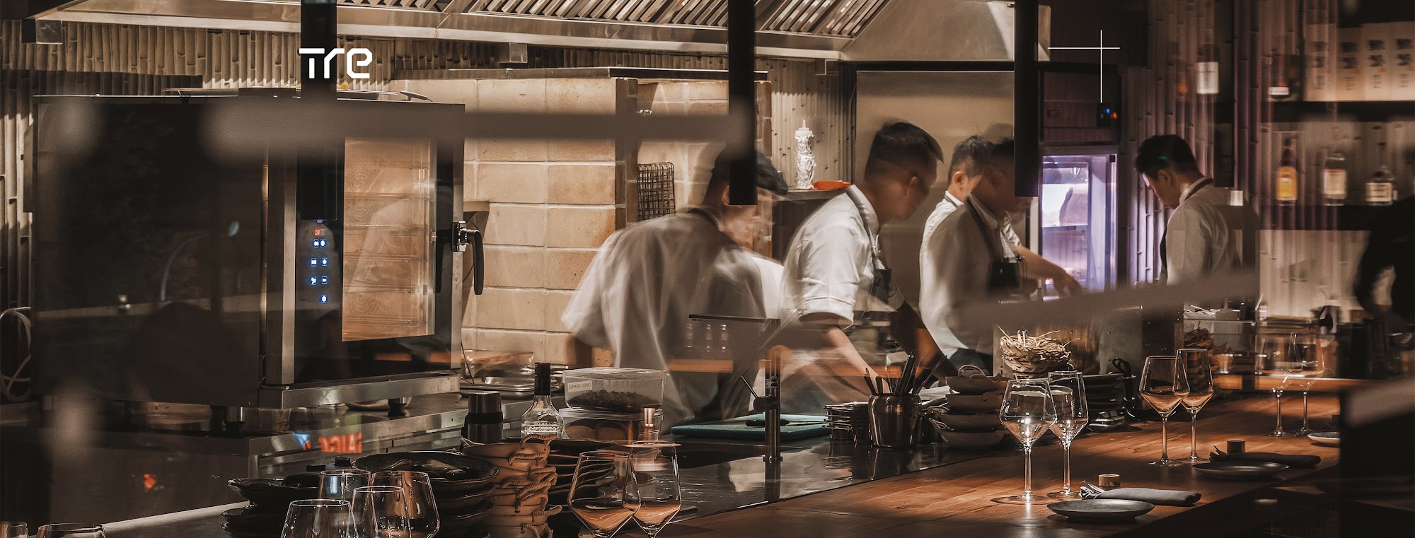 The image depicts the interior of a restaurant kitchen in Thao Dien, Saigon. It features multiple chefs in white uniforms working at a counter, with v
