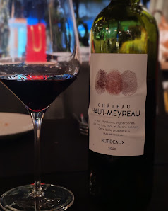 A bottle of Chateau Haut-Meyreau Bordeaux wine from the year 2013 is placed on a table next to a glass filled with red wine, indicating that it has be