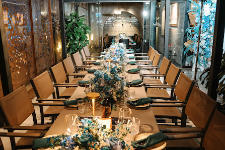 The image shows a long dining table set up in an elegant interior space, likely within a restaurant or event venue. The tables are adorned with blue a