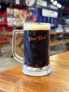 A close-up of a dark beer in a glass mug labeled 'Beer Hall' on top of a wooden table.
