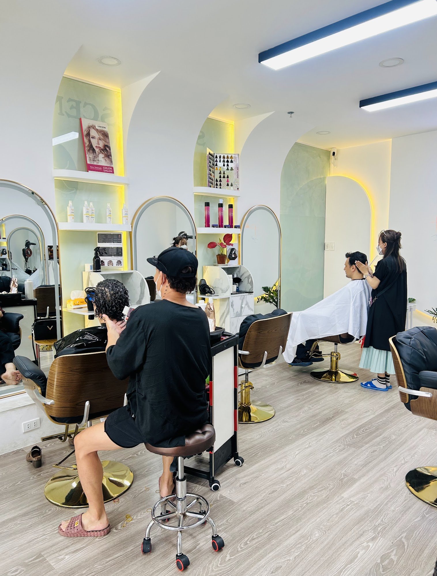 The image depicts an interior view of a modern hair salon located in Thao Dien, Saigon. The space is well-lit with overhead lights and features arched