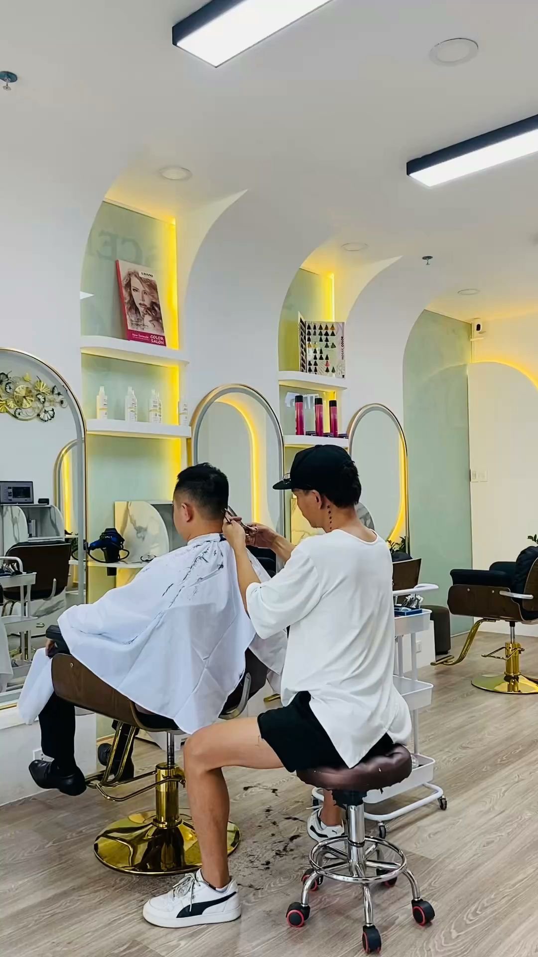 The image depicts an interior view of a modern hair salon located in Thao Dien, Saigon. The setting includes contemporary styling chairs with gold and