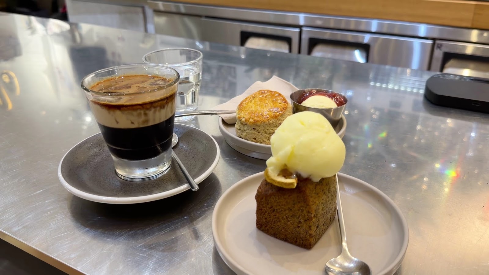 A slice of cake with ice cream on top, served alongside a cup of coffee and scones with butter and jam. The dessert appears to be a classic British-style afternoon tea.