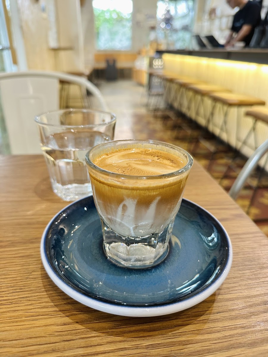 A close-up shot of a glass containing an espresso-based coffee drink on a blue saucer with ice cubes at the bottom, placed in front of two glasses fil