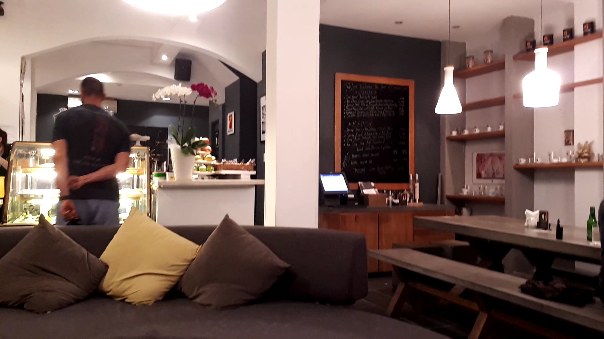 The image depicts an indoor setting of a cafe or restaurant in Thao Dien, Saigon. The foreground shows a comfortable seating area with cushions on a c
