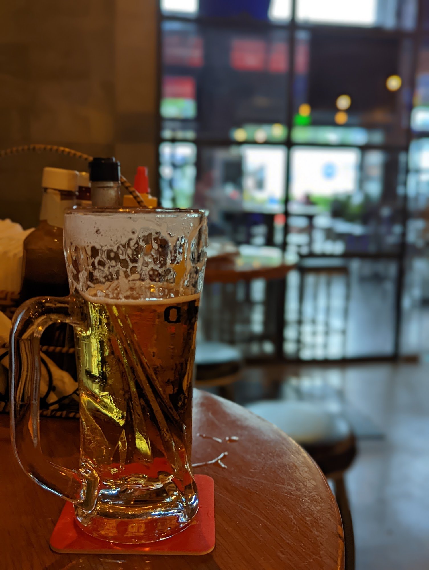 A close-up of a large mug filled with beer on a coaster at an indoor venue.