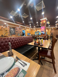 The image shows an interior view of a restaurant featuring wooden tables and chairs arranged in rows with red upholstered booths along the wall. The d