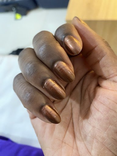 A close-up of a person's hand displaying nails painted in metallic shades of brown and gold.