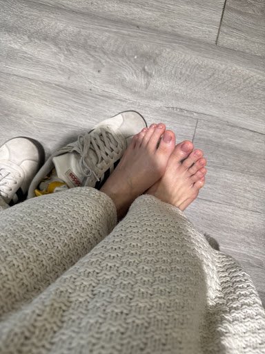 A close-up view of a person's feet wearing white sneakers and beige knitted socks on grey wooden flooring.