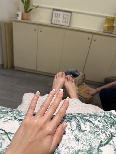 The image shows a person's feet resting on an ottoman in what appears to be a living room or lounge area, with another individual seated further back 