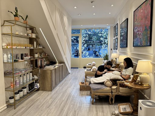 The image depicts an interior view of a modern and well-lit spa or wellness center with two individuals receiving treatments on reclining chairs, surr