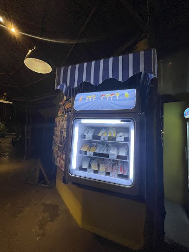 The image shows a vending machine inside what appears to be an indoor venue at night time. The vending machine is illuminated from within and displays