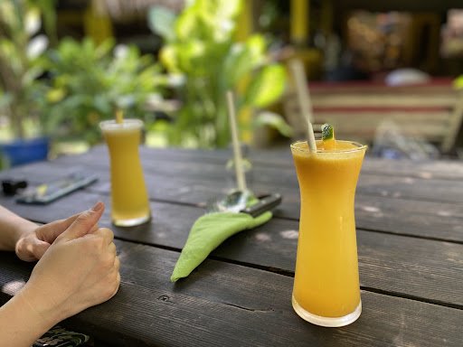 The image shows a wooden table on which there are three glasses filled with an orange-colored beverage that appears to be mango juice or a similar tro