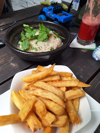The image shows a plate of golden-brown French fries on the right side and a bowl containing rice with garnishes, possibly cilantro and carrots, in th