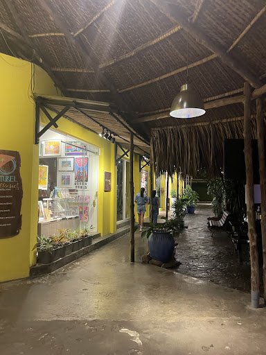 The image shows an exterior view of a restaurant or cafe at night time. The establishment has yellow walls and is covered with thatched roofing, givin