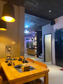 The image shows an interior view of a modern dining area featuring wooden tables and chairs with built-in induction cooktops, pendant lighting fixture
