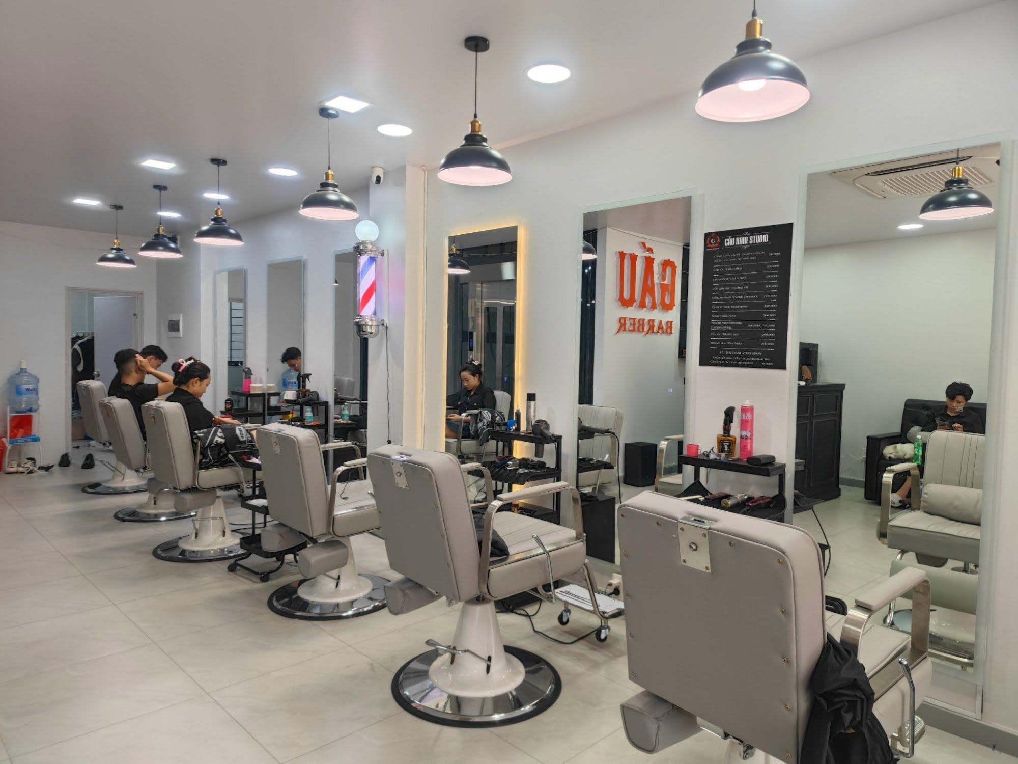 The image shows an interior view of a modern barber shop named 'GAS Barber Shop'. The salon is well-lit with overhead and pendant lights, featuring wh