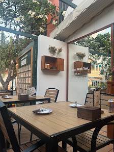 Exterior view of a café or restaurant in Thao Dien, Saigon. Features include wooden tables and chairs arranged for outdoor seating, a white wall with 
