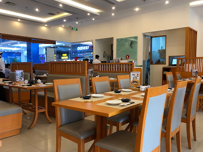 The image depicts the interior of a modern restaurant located in Thao Dien, Saigon. It features neatly arranged wooden tables with gray cushioned chai