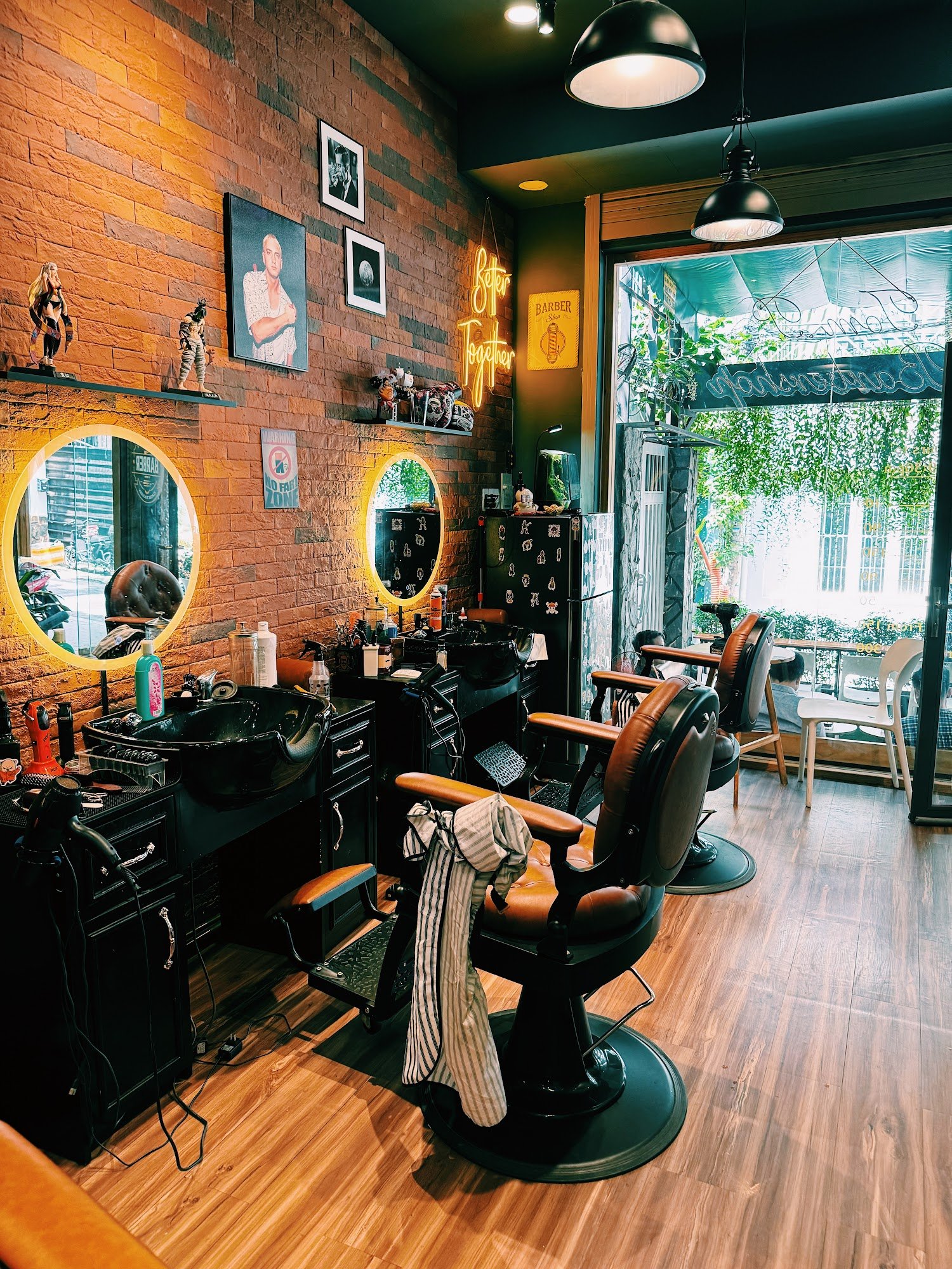 Interior of a barber shop with exposed brick walls, circular illuminated mirrors, vintage-style barber chairs, black sinks, neon sign reading 'Better