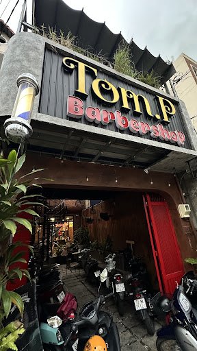The image shows an exterior view of a barber shop named 'Tom.P Barber Shop'. The establishment is located in Thao Dien, Saigon and has a distinctive s