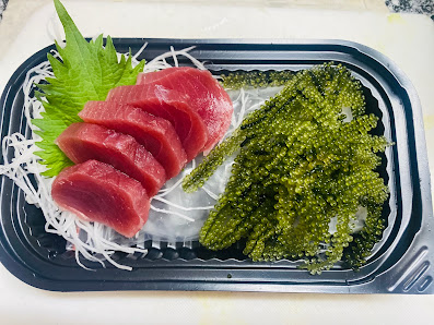 The image shows a food item consisting of raw tuna slices and seaweed served on ice in a plastic container.