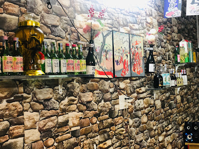 The image shows an interior wall of a venue adorned with various bottles on shelves and colorful paintings hanging above the stone wall.