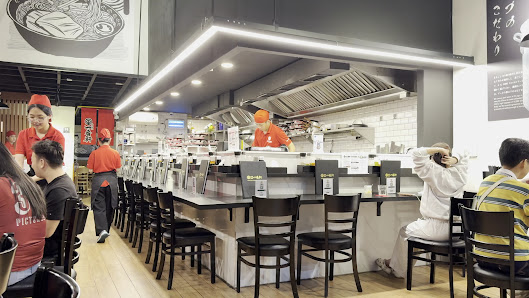 The image depicts the interior of a restaurant located in Thao Dien, Saigon. It features a modern dining area with black bar stools arranged along a l
