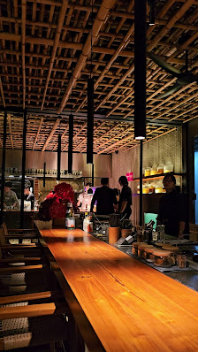 The image depicts an interior view of a modern restaurant or bar setting featuring wooden beams on the ceiling and warm lighting from pendant lamps ab