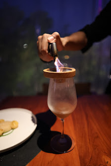 A person is using a lighter to ignite the contents of a glass container placed on top of another vessel filled with liquid, possibly creating an effec