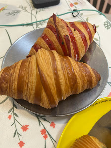Two croissants on a metal plate; one is plain and the other has red stripes possibly indicating some kind of topping or glaze.