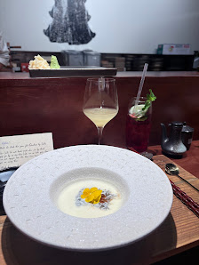 A restaurant table in Thao Dien, Saigon, featuring a white plate with a creamy dish and a yellow garnish, a glass of white wine, a red cocktail with a
