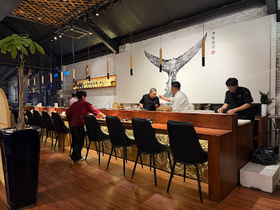 The image depicts the interior of a restaurant in Thao Dien, Saigon. It features a long wooden counter with black chairs, several people interacting (