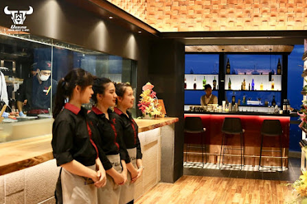 The image depicts the interior of a modern restaurant in Thao Dien, Saigon. Three female staff members in black uniforms with red accents stand near a