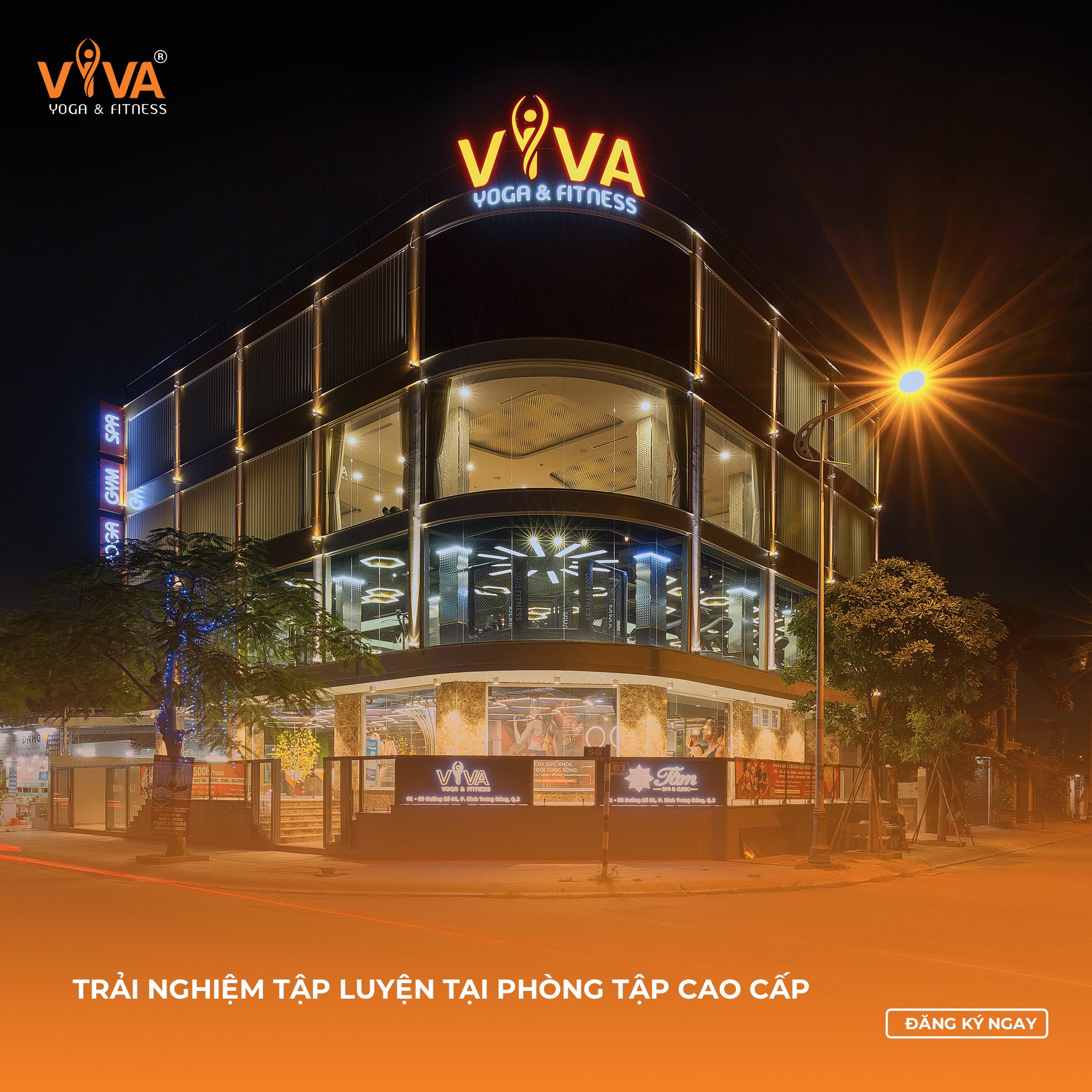 The image shows an exterior view of a modern fitness center at night time-lit with bright lights and signage that reads 'VIVA Yoga & Fitness'. The bui