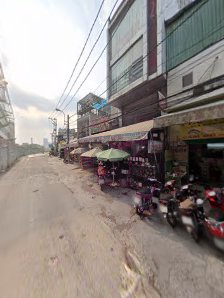 The image depicts a street view of an urban area with several small shops and stalls on the side of the road, motorcycles parked along the curb, and b